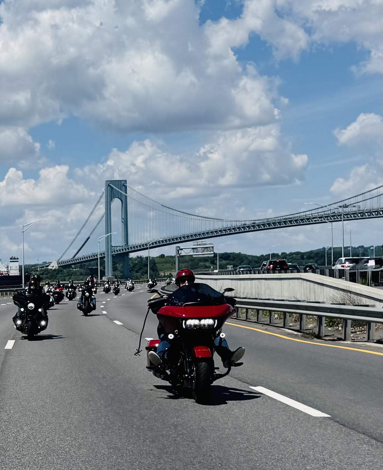 A line of motorcycles driving on a highway with a bridge in the background