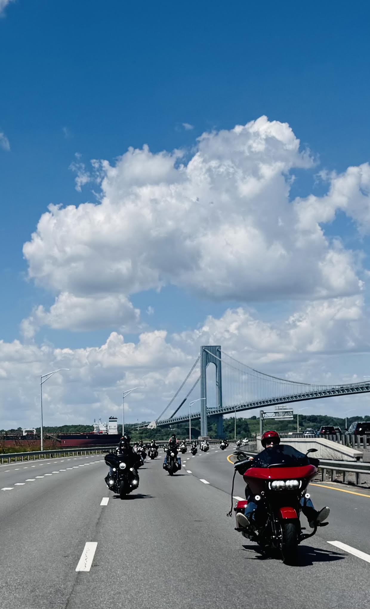 A line of motorcycles on a highway with a bridge in the background