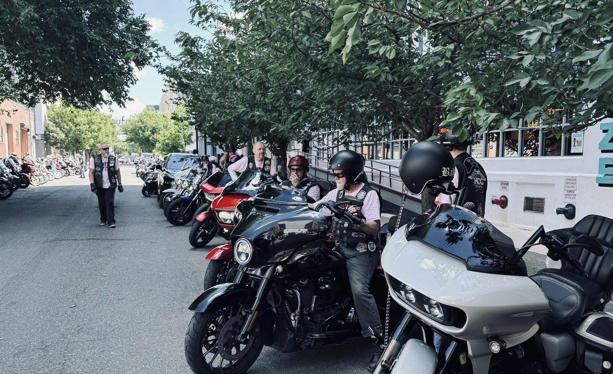 People on motorcycles parked on a tree-lined street