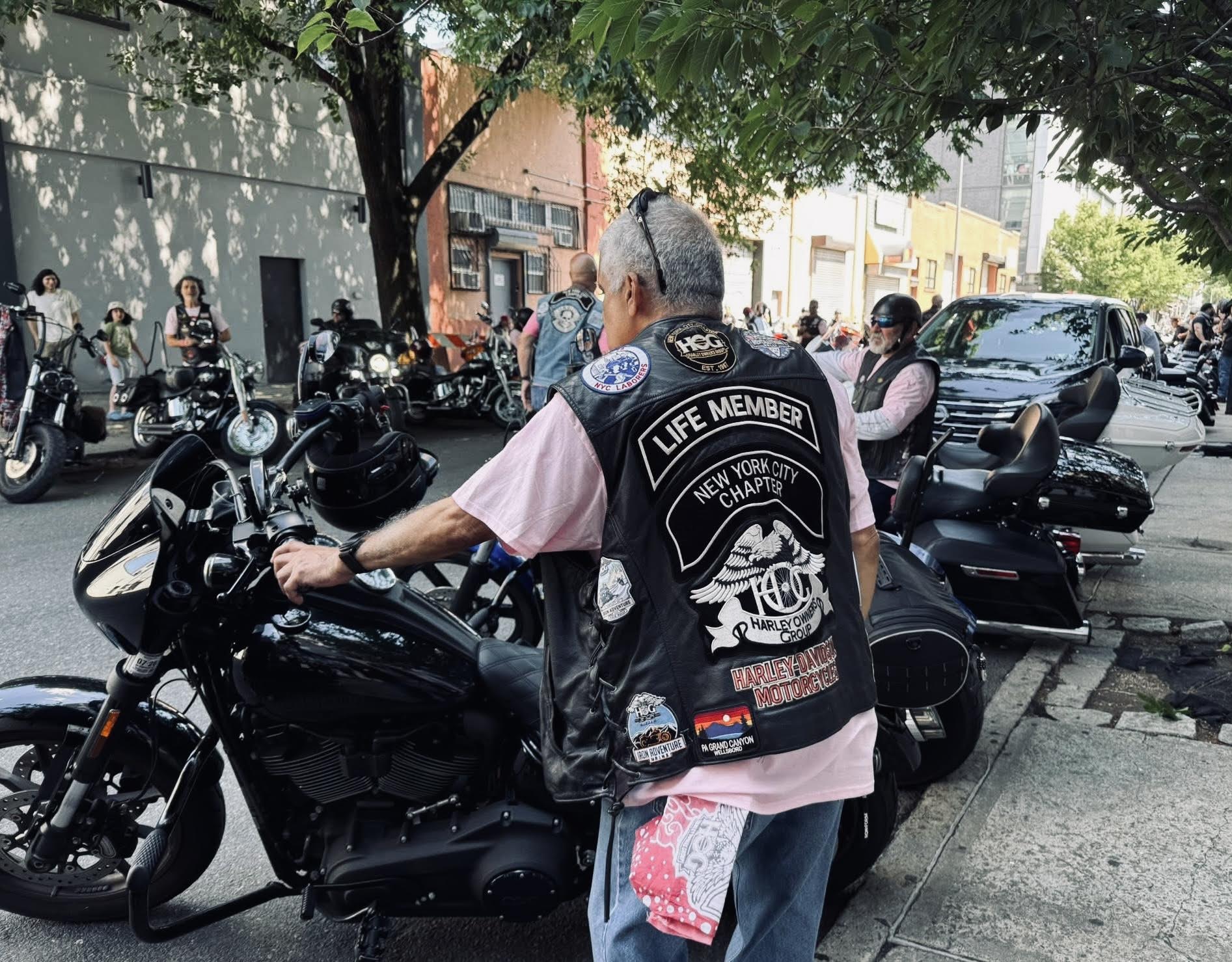 Motorcycle riders in pink shirts and leather jackets with their motorcycles lining a street