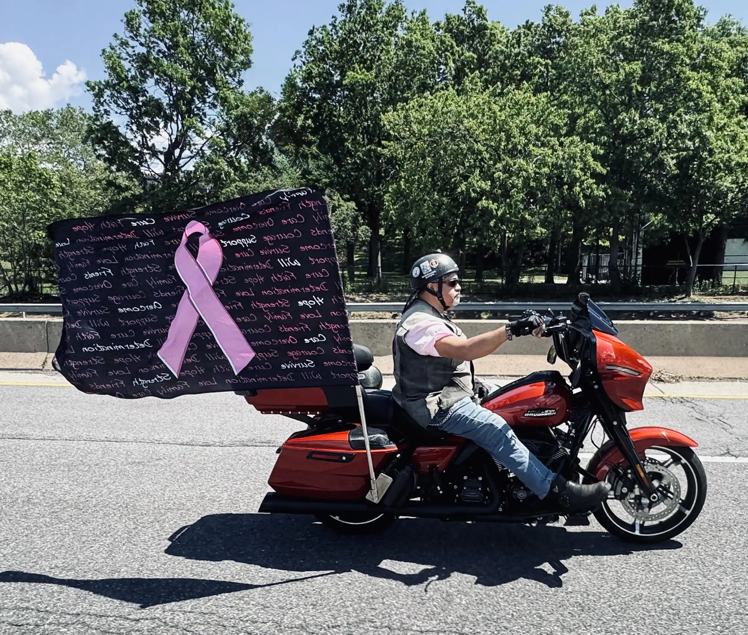 Man riding a red motorcycle with a breast cancer flag flying