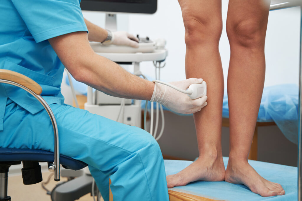 Medical worker sitting in chair carefully examining the patient's legs using an ultrasound machine
