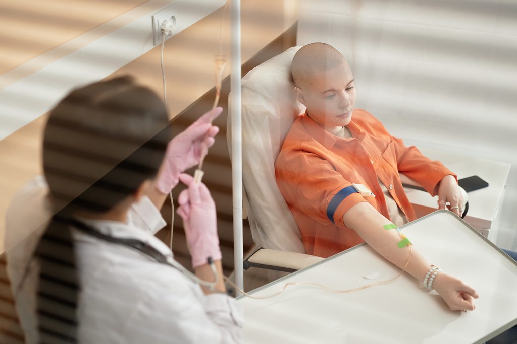 High angle portrait of bald young woman receiving chemotherapy treatment in procedure room at clinic behind glass copy space
