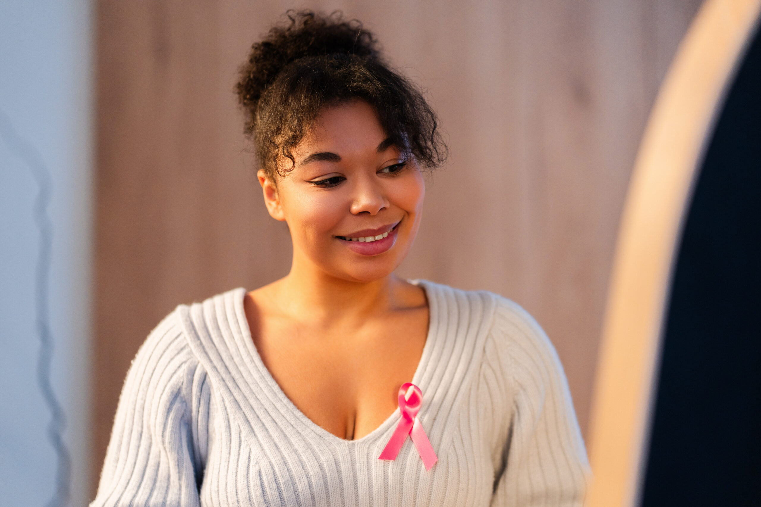 African american woman wearing gray sweater and pink breast cancer ribbon
